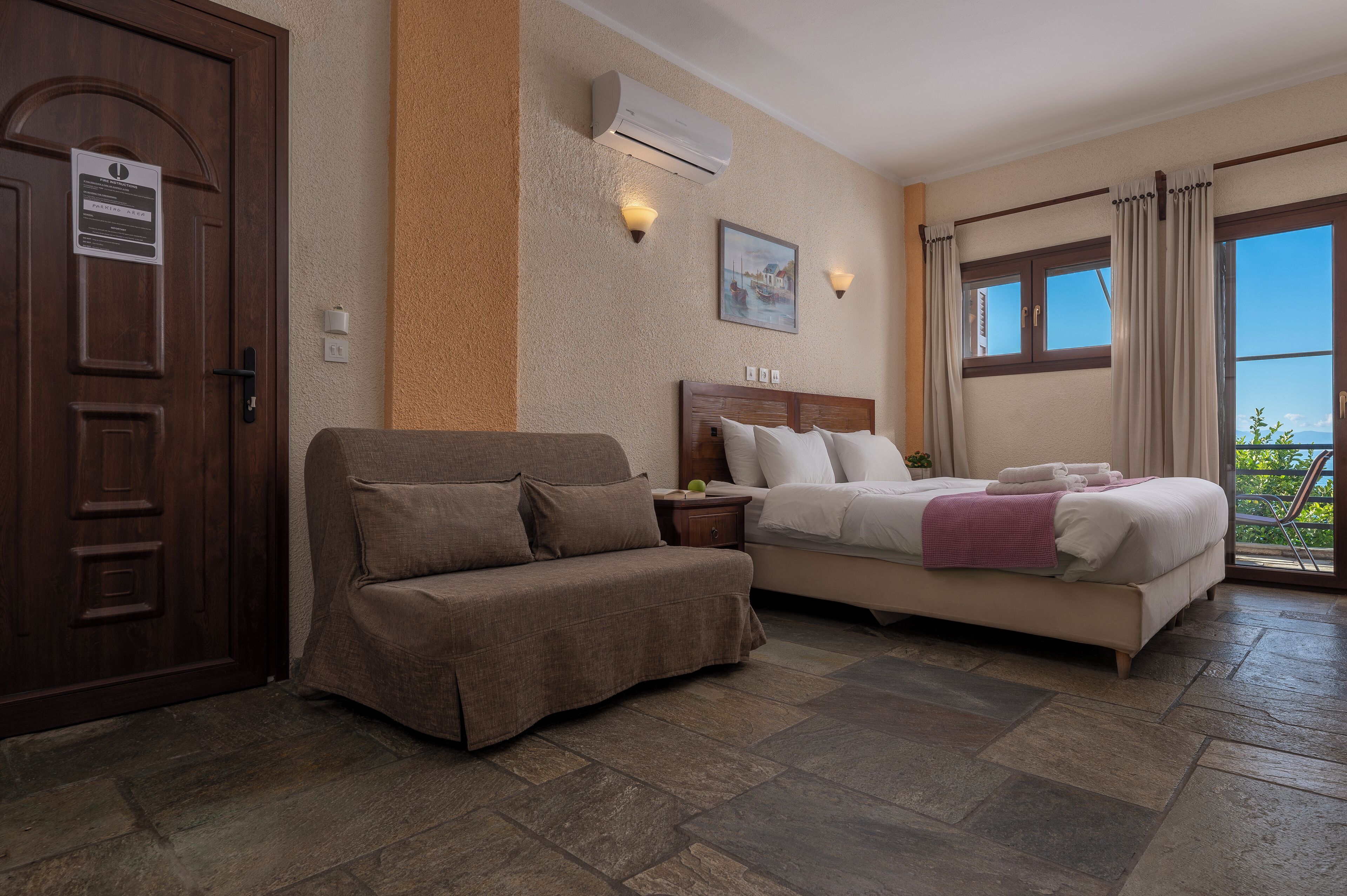 Una habitación de hotel con una cama, un sofá, una puerta de madera y una ventana con cortinas.