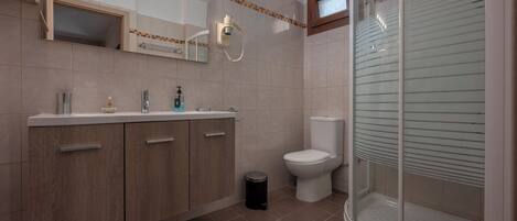 Une salle de bain équipée d’un meuble-lavabo, de toilettes et d’une douche à parois de verre.