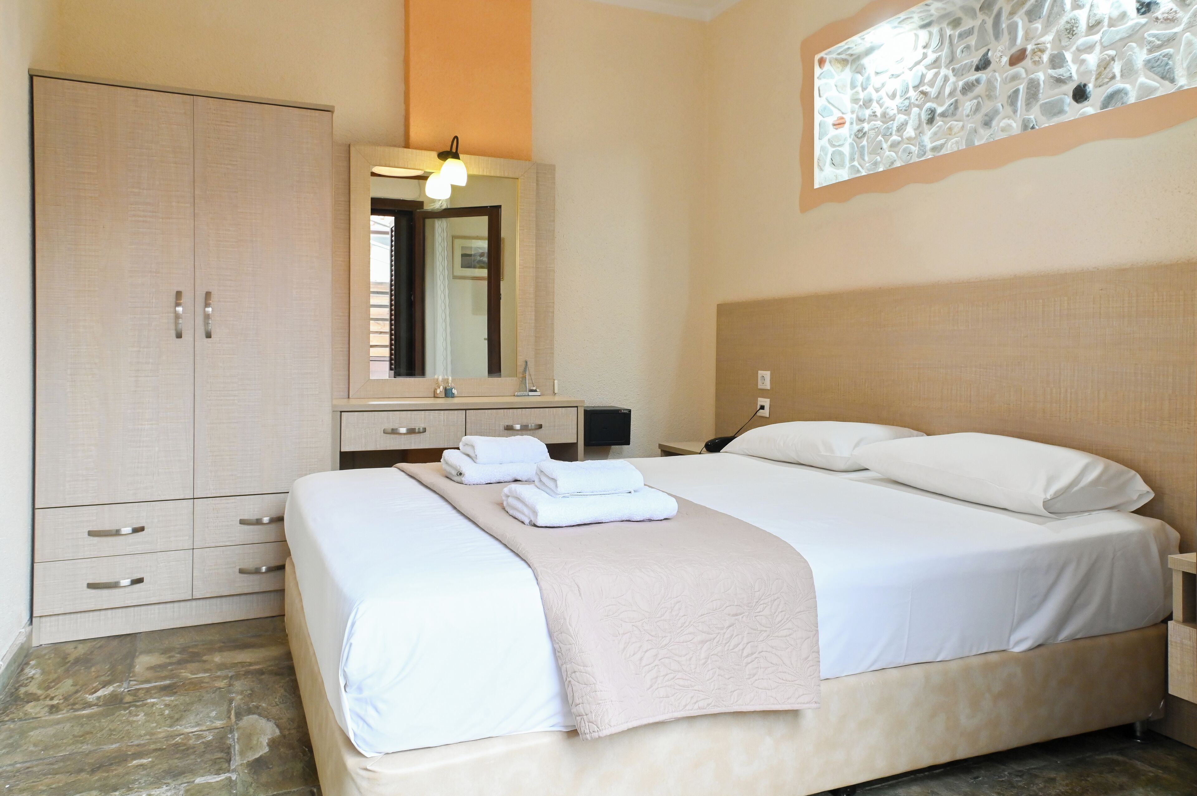 A neatly arranged bedroom with a bed, a wardrobe, a nightstand, and a mirror.