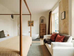 A bedroom with a four-poster bed, a white sofa, a wooden cabinet, and a large window. - Holm Somerset (South Petherton)