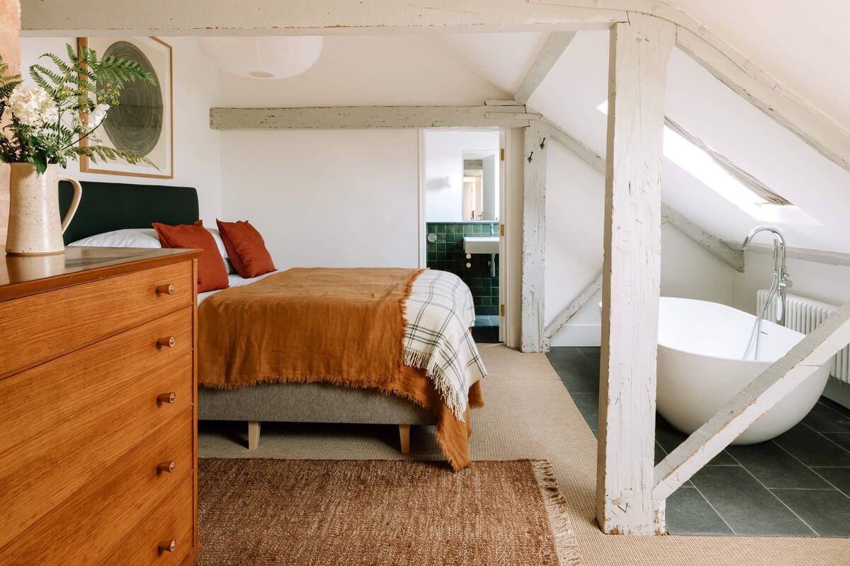 A bedroom with a bed, dresser, and a view of a bathroom with a bathtub.