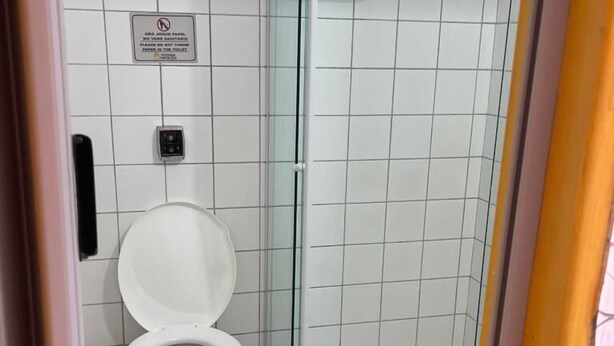 A small, tiled bathroom with a toilet and a glass shower enclosure. - Pousada Fortaleza (Paraty)
