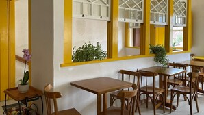 A dining area with yellow-framed windows, wooden tables and chairs, and potted plants. - Pousada Fortaleza (Paraty)
