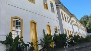 Un edificio blanco con puertas y ventanas amarillas, rodeado de follaje.