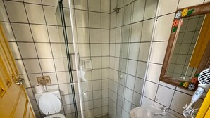 A bathroom with a toilet, a shower enclosure, a sink, and a mirror. - Pousada Fortaleza (Paraty)