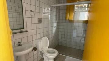 A bathroom with white tiled walls, a white sink, a toilet, and a shower area.