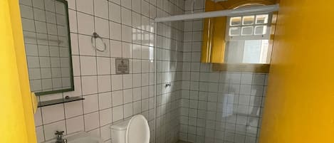 A bathroom with white tiled walls, a white sink, a toilet, and a shower area.