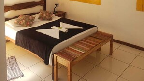 A bedroom with a bed, a bench, a window with yellow shutters, an air conditioning unit, and a ceiling fan. - Pousada Fortaleza (Paraty)