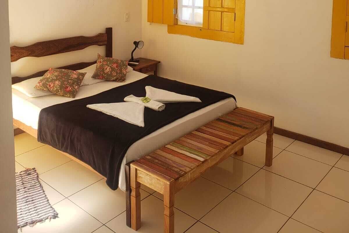 Ein Schlafzimmer mit einem Bett, einer Bank, einem Fenster mit gelben Rollläden, einer Klimaanlage und einem Deckenventilator.