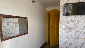 Habitación de hotel con un espejo grande, un televisor de pantalla plana en la pared, una puerta de madera y un papel tapiz estampado.
