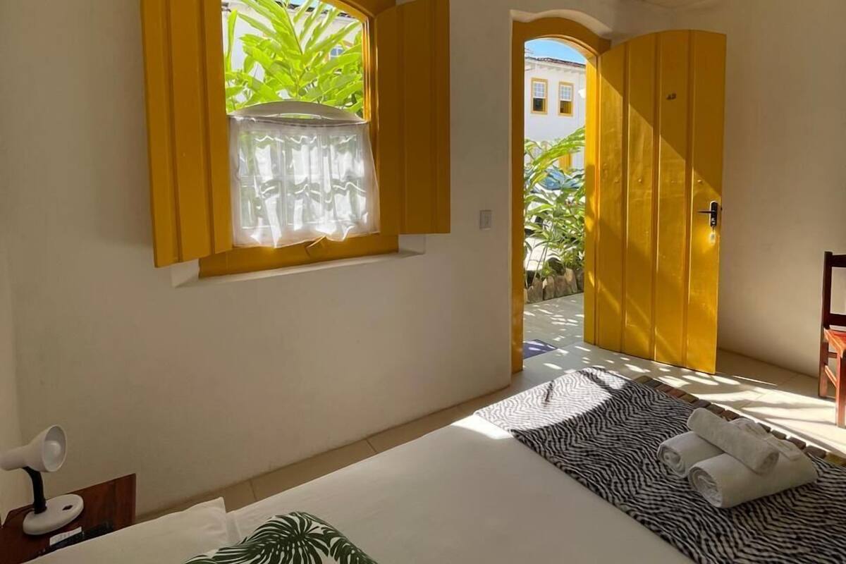 Ein Schlafzimmer mit Bett, einem Fenster mit Vorhängen, einem Deckenventilator und einer zur Außenseite führenden Tür.