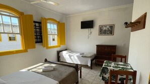 A room with two single beds, a desk with a chair, a television, and a window with yellow shutters. - Pousada Fortaleza (Paraty)