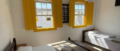 A hotel room with two beds, a ceiling fan, and windows with yellow shutters.