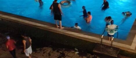 Una piscina con gente nadando y tomando el sol en el borde.
