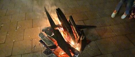 A fire pit with burning logs on a paved surface.