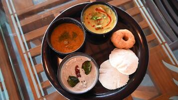 Une assiette noire avec trois bols de nourriture et deux « idlis ».