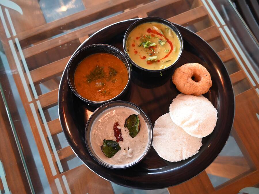 Une assiette noire avec trois bols de nourriture et deux « idlis ».