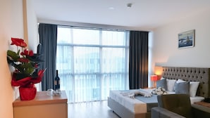 A hotel room with a bed, a sofa, a desk with a lamp, a potted plant, and a large window with curtains. - Lara Street Hotel (Antalya)