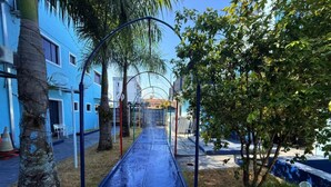 A blue building with a covered outdoor area, including a slide and a pathway lined with trees. - Hotel Mais Lazer (Joinville)