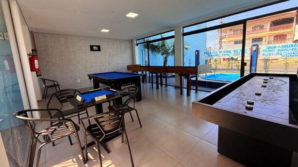 A pool table, chairs, and a foosball table in a well-lit room with large windows. - Hotel Mais Lazer (Joinville)