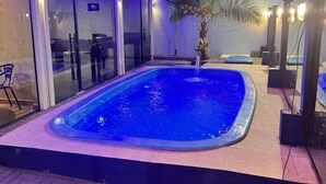 A swimming pool with a tiled deck, surrounded by glass doors and a palm tree. - Hotel Mais Lazer (Joinville)