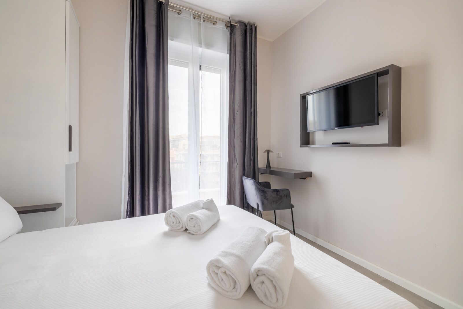 A hotel room with a bed, a TV mounted on the wall, and a desk with a chair.