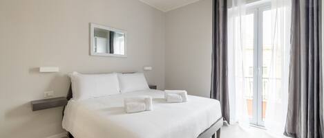 Habitación de hotel moderna con una cama grande, una mesita de noche, un espejo y vistas al balcón exterior.