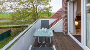 A balcony with a glass table and chairs, a brick wall, and a view of a green landscape. - Vacation apartment Deichblick with sauna (Norddeich)
