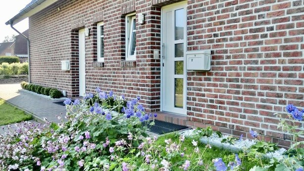 A brick building with a modern design, featuring a large window and a door. - Vacation apartment Deichblick with sauna (Norddeich)