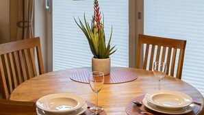 A round wooden dining table with two chairs, a potted plant, and a wine glass. - Vacation apartment Sea Breeze (Norden)