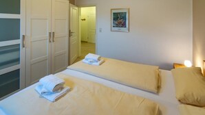 A hotel room with two beds, each with a neatly folded towel, a framed picture on the wall, and a door leading to another room. - Vacation apartment Sea Breeze (Norden)