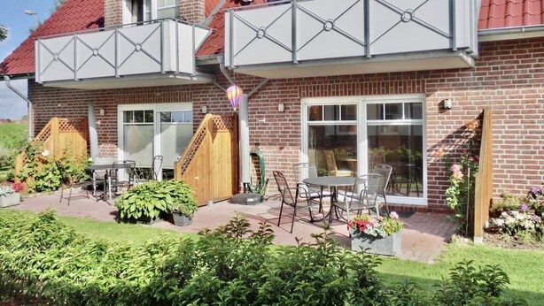A two-story house with a brick exterior, a balcony with a metal railing, and a patio with outdoor furniture. - Vacation apartment Sea Breeze (Norden)