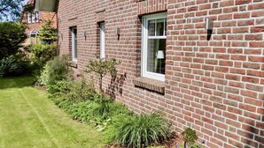 A brick building with a well-maintained garden and a small window with a white frame. - Vacation apartment Sea Breeze (Norden)