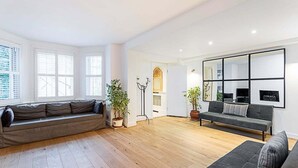 A spacious living room with a grey sofa, a black sofa, and a wooden floor. There are two potted plants and a large mirror on the wall. - Richmond Hill Top Apartment (London)