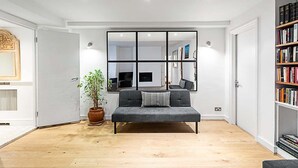 A modern living room with a grey sofa, a large mirror, and a bookshelf. - Richmond Hill Top Apartment (London)