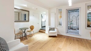 A spacious living area with a wooden floor, a dining table with chairs, a white armchair, and a large mirror. - Richmond Hill Top Apartment (London)
