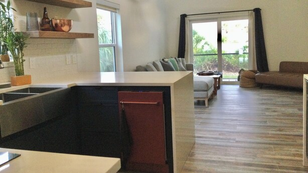 Una cocina moderna con isla integrada, un rincón de comedor con sofá y un amplio ventanal corredero hacia el exterior.
