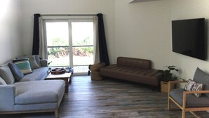 Una sala de estar con un sofá gris, un sofá marrón, una mesa de centro de madera y un televisor montado en la pared.