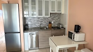 Una cocina moderna con armarios blancos, un refrigerador de acero inoxidable, un microondas y una cafetera sobre la encimera.
