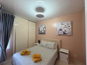 Un dormitorio con una cama, una mesita de noche, una lámpara de pared y dos cuadros de flores.