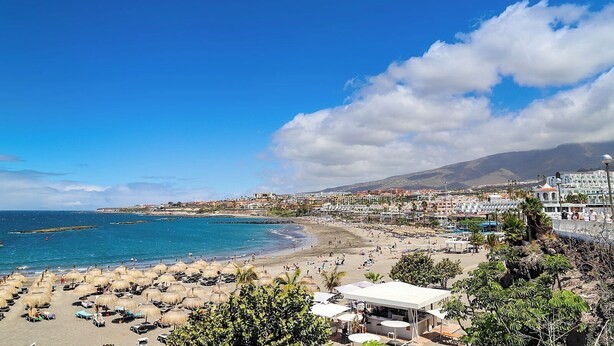Un pueblo costero con playa, sombrillas de paja y un puerto deportivo.