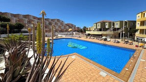 Una piscina con plataforma de baldosas, rodeada de edificios con balcones y un cielo despejado.