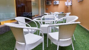 Ein Patio mit weißen Korbmöbeln, Tischen, Klimaanlagen an der Wand und einem Glastür-Eingang.
