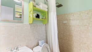 A bathroom with a sink, toilet, and shower. There is a mirror above the sink and a shelf with towels. - The Ocean View Inn & Pub (Islamorada)