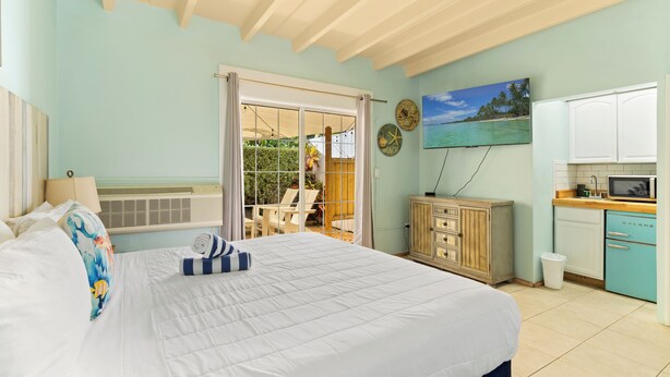 A bedroom with a large bed, a sliding glass door to a balcony, a wooden cabinet, and a kitchen area with a microwave. - The Ocean View Inn & Pub (Islamorada)