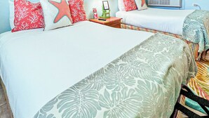 A hotel room with two beds, each with a different patterned bedspread, a nightstand with a lamp, framed artwork on the wall, and an air conditioning unit. - The Ocean View Inn & Pub (Islamorada)