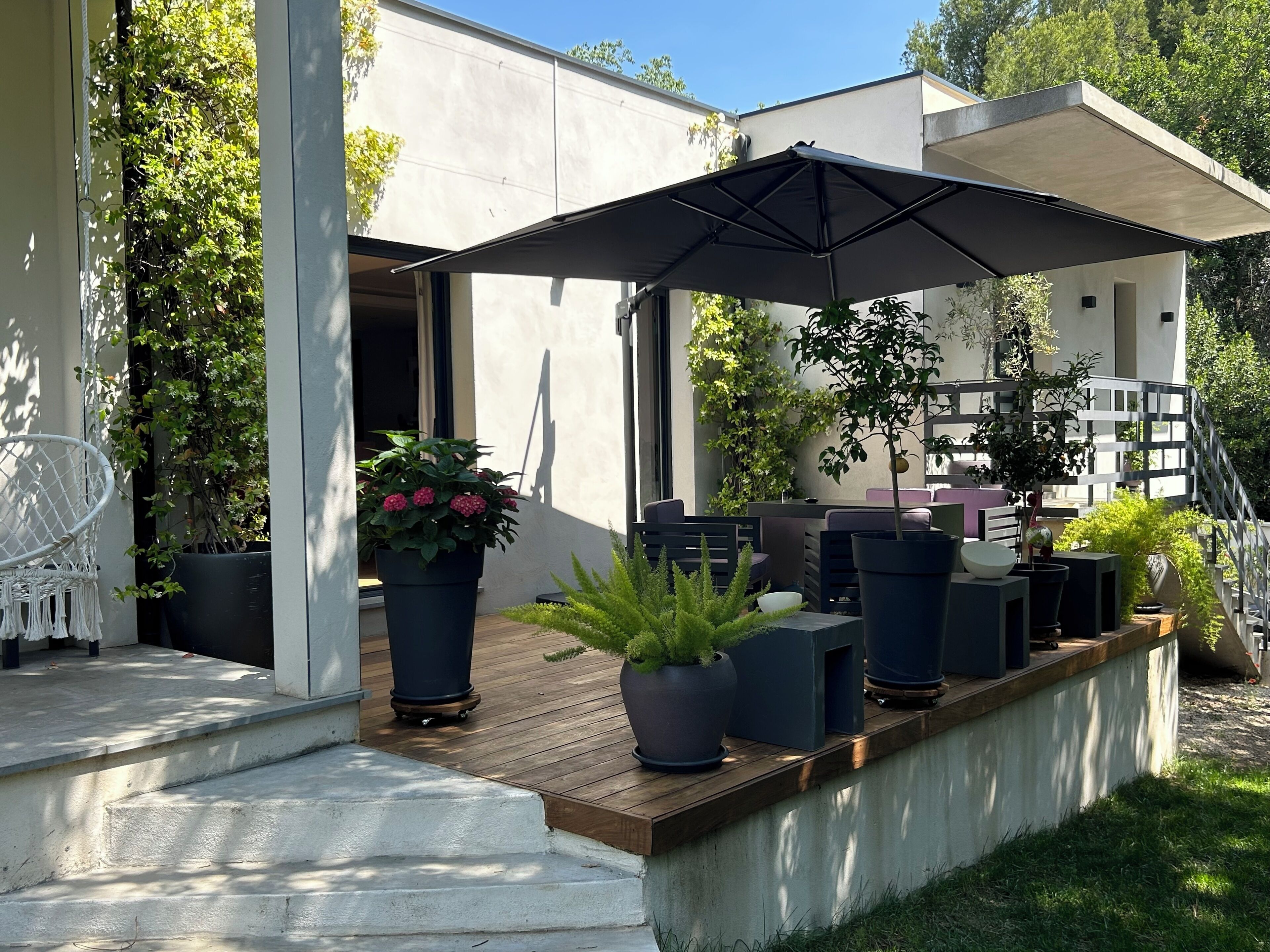 Um pátio moderno ao ar livre com deck de madeira, plantas em vasos e móveis de jardim.