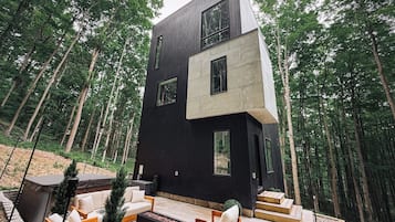 Una casa moderna de dos pisos con un patio que incluye mobiliario exterior y una chimenea.