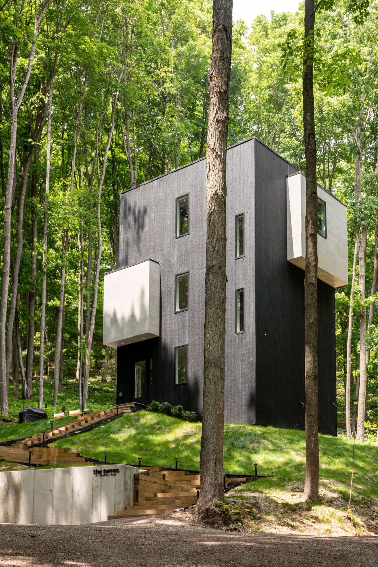 A modern, two-story building with a flat roof, surrounded by a forest.