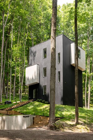 A modern, two-story building with a flat roof, surrounded by a forest.